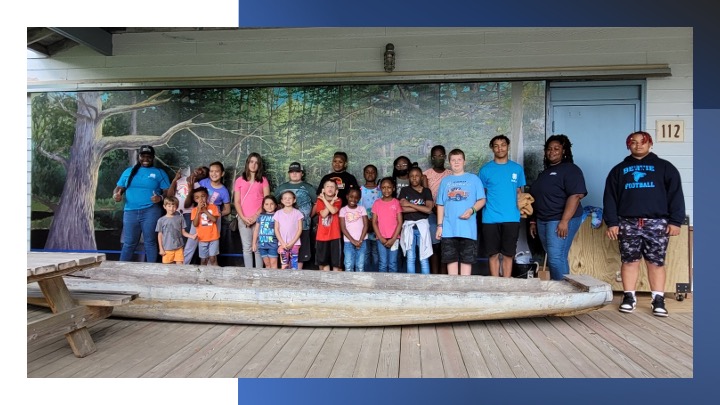 Kids stand with a wooden canoe.