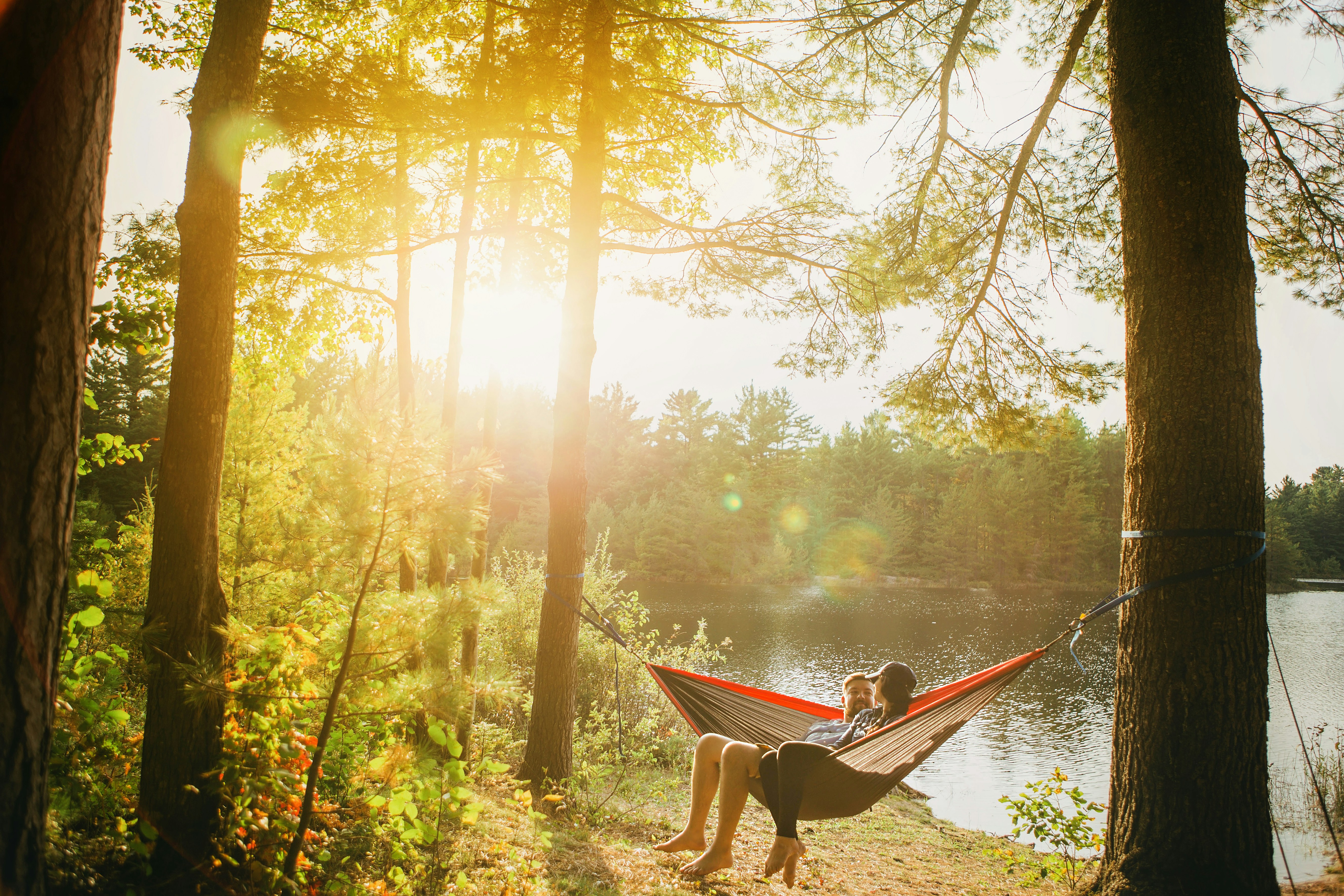 A man and woman relaxing together in a hammock outdoors by a lake, enjoying nature without digital devices.