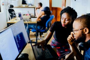 A female educator helps a male student navigate a technical issue on his laptop.