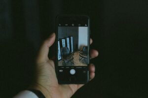 Hand holding a smartphone displaying a photo of two chairs and vertical signs in a dark indoor setting.